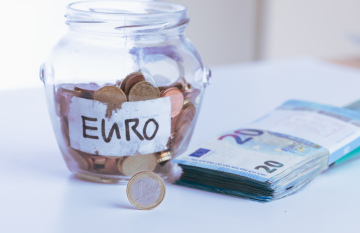 Euro coins in a glass jar and a bundle of banknotes