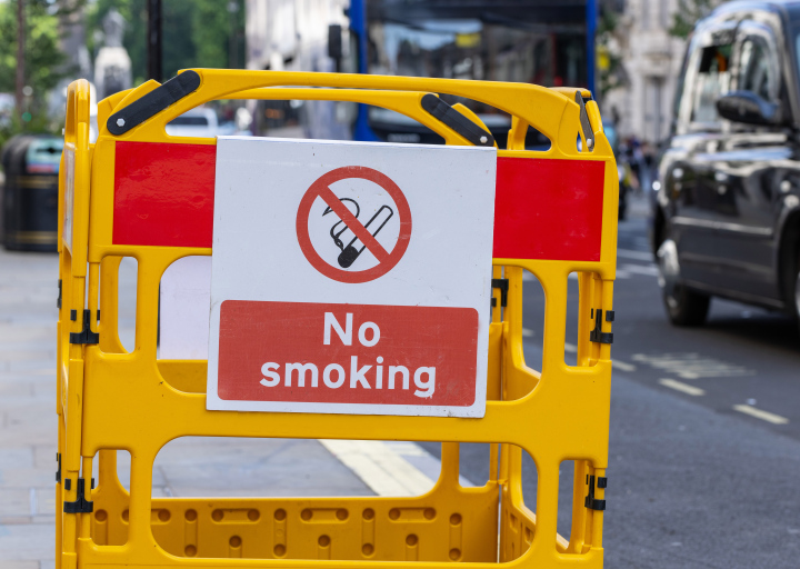 No Smoking, inscription in English on warning board, busy street.